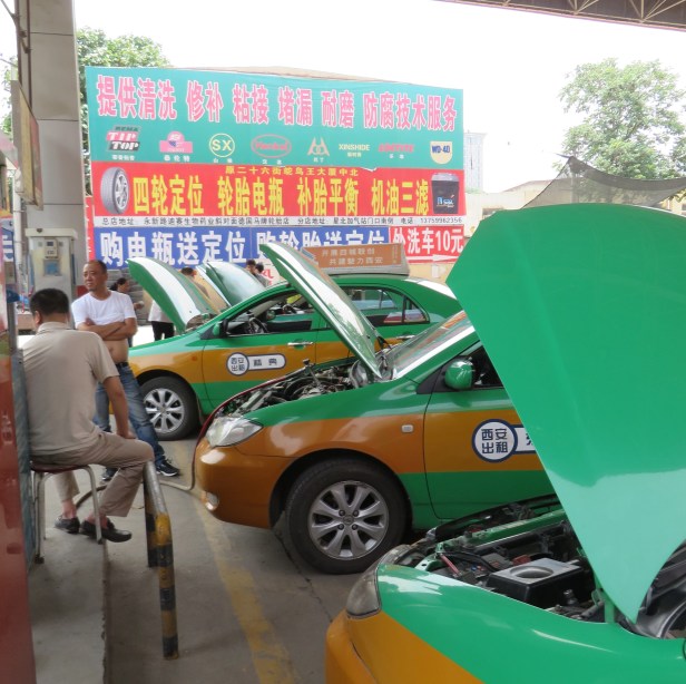 Many taxis have been converted to natural gas, crowd the fueling station and raise their hoods to fill up.