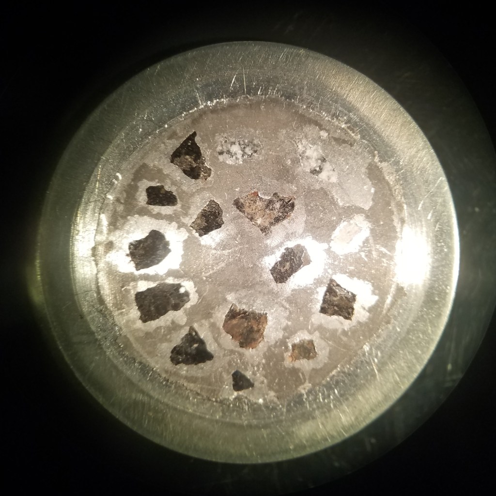 Aluminum mount with meteorite chips embedded in indium (soft metal). Aubrites are in the top right third, EH chondrites in the top left third, and EL chondrites in the bottom third.