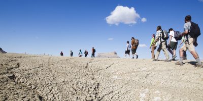 A large group hikes across a barren shale formation in Utah.